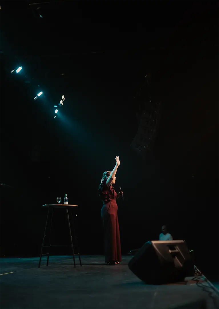 Euza Bispo no palco, iluminada por refletores, durante uma palestra.