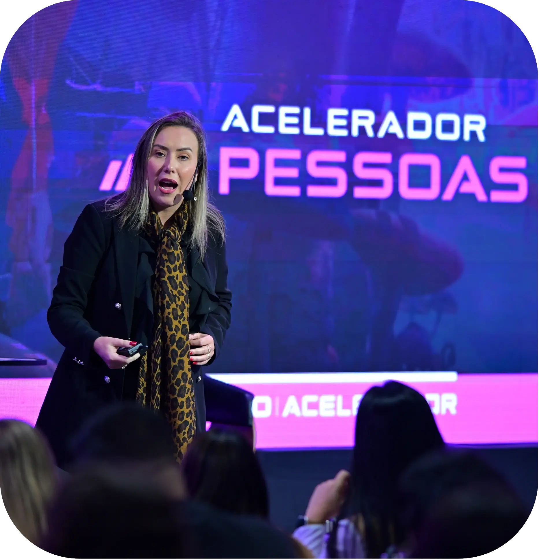 Euza Bispo de blazer preto apresentando em um palco, com o público em primeiro plano.